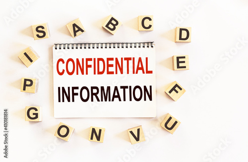 CONFIDENTIAL INFORMATION is written on a notebook next to wooden cubes with letters. Business concept