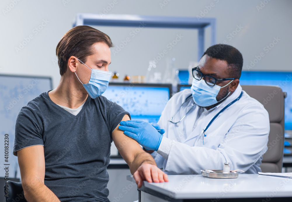 Fototapeta premium African-American doctor makes a coronavirus vaccine using a syringe and hypodermic needle. Professional medical worker and patient at the hospital office. Vaccination and safety.
