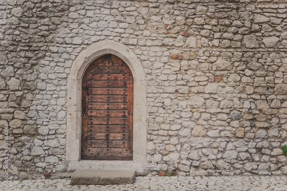 Ancient wooden arcade door with iron rivets at wall of old building. Heavy closed door on a stone wall of a medieval fortress, made of riveted wood planks. Small back door to Wawel castle in Krakow. Ancient wooden arcade door with iron rivets at wall of old building. Heavy closed door on a stone wall of a medieval fortress, made of riveted wood planks. Small back door to Wawel castle in Krakow.