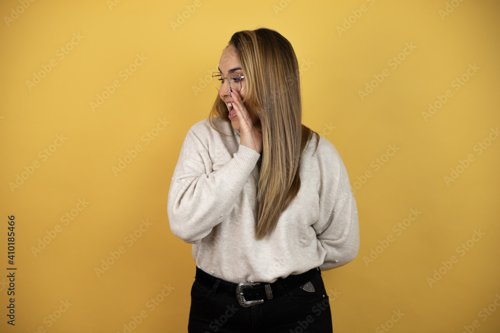Pretty woman with long hair with hand on mouth telling secret rumor, whispering malicious talk conversation against yellow wall Pretty woman with long hair with hand on mouth telling secret rumor, whispering malicious talk conversation against yellow wall