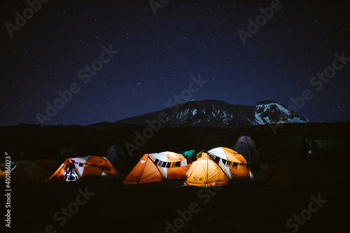 row of orange lit tents at Kilimanjaro at night summit visible in the background for a corporate annual report magazine cover profitable table
