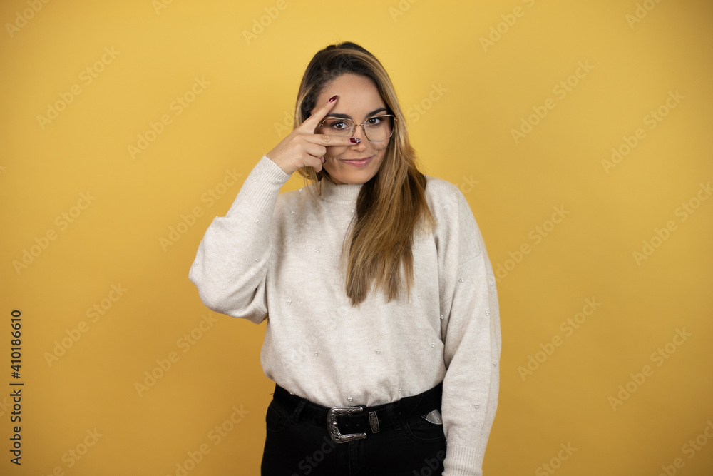 Pretty woman with long hair peeking in shock covering face and eyes with hand, looking through fingers with embarrassed expression against yellow wall Pretty woman with long hair peeking in shock covering face and eyes with hand, looking through fingers with embarrassed expression against yellow wall