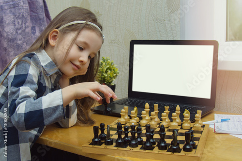 Mock-up online chess courses for children. Child with a chessboard and laptop. Little girl plays chess on the internet. Games for the development of the brain and useful time in the quarantine.