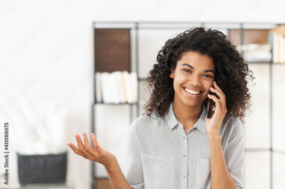 Smiley African American teenage girl with curly hair talking on mobile phone,chatting with friend or family, young joyful businesswoman having pleasant conversation, discussing project with the client Smiley African American teenage girl with curly hair talking on mobile phone,chatting with friend or family, young joyful businesswoman having pleasant conversation, discussing project with the client