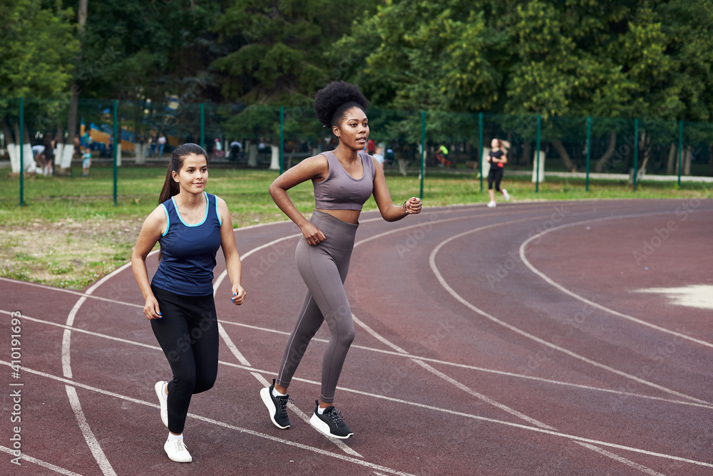 Fototapeta premium Two young girls go in for sports at the stadium. Jogging in the open air