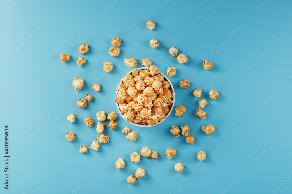 Caramel popcorn in a white glass cup with scissors on a blue background Caramel popcorn in a white glass cup with scissors on a blue background