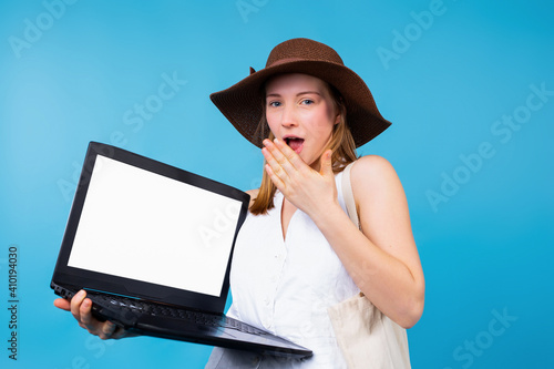 Shocked surprised woman wearing white t-shirts holding hand closing mouth with a laptop pc computer, blank screen mockup copy space isolated on blue background, studio portrait with side space