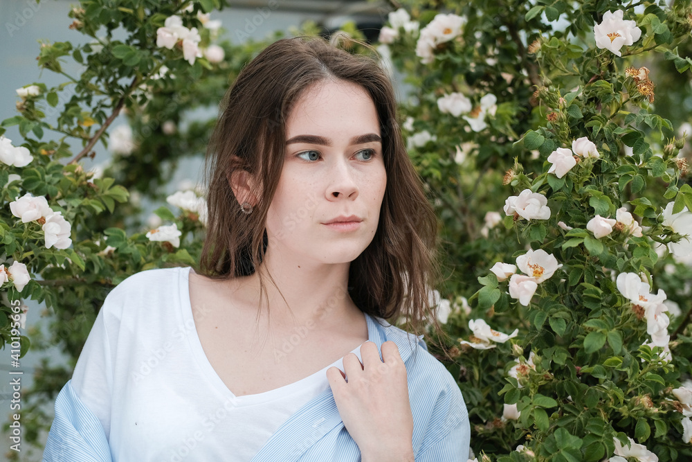 a girl in a white shirt with clear skin on her face. on the background of a rosehip bush a girl in a white shirt with clear skin on her face. on the background of a rosehip bush