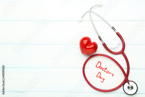 Stethoscope with red heart and text Doctor's Day on white wooden table © 5second