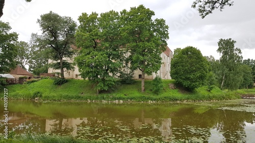 Latvian castle Jaunpils behind green trees on the shore of a small lake on July 12, 2019