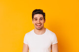 Brunette guy in white T-shirt smiles and looks into camera on orange background