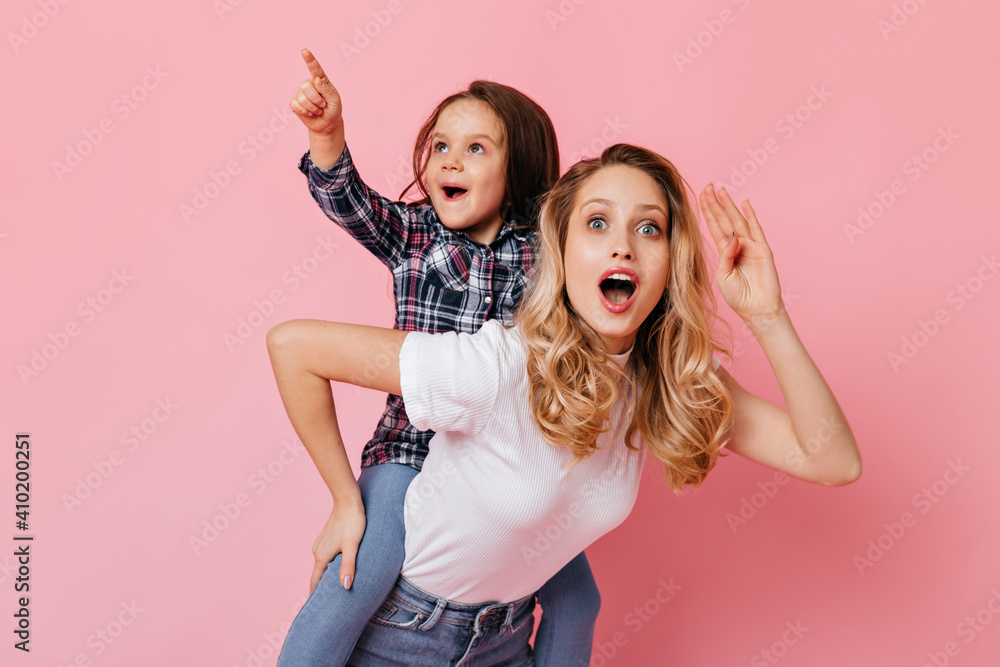 Blue-eyed woman stares in amazement at camera, holding daughter on her back, wearing plaid shirt Blue-eyed woman stares in amazement at camera, holding daughter on her back, wearing plaid shirt