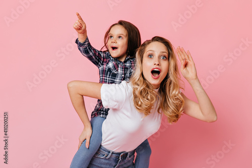 Blue-eyed woman stares in amazement at camera, holding daughter on her back, wearing plaid shirt