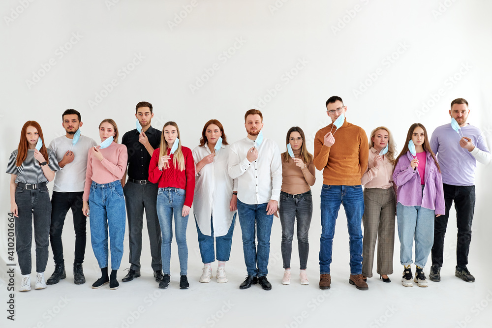 Obraz premium men and women wearing medical face mask, stand in a row posing looking at camera, isolated over white studio background. global society. disease epidemic, coronavirus infection concept