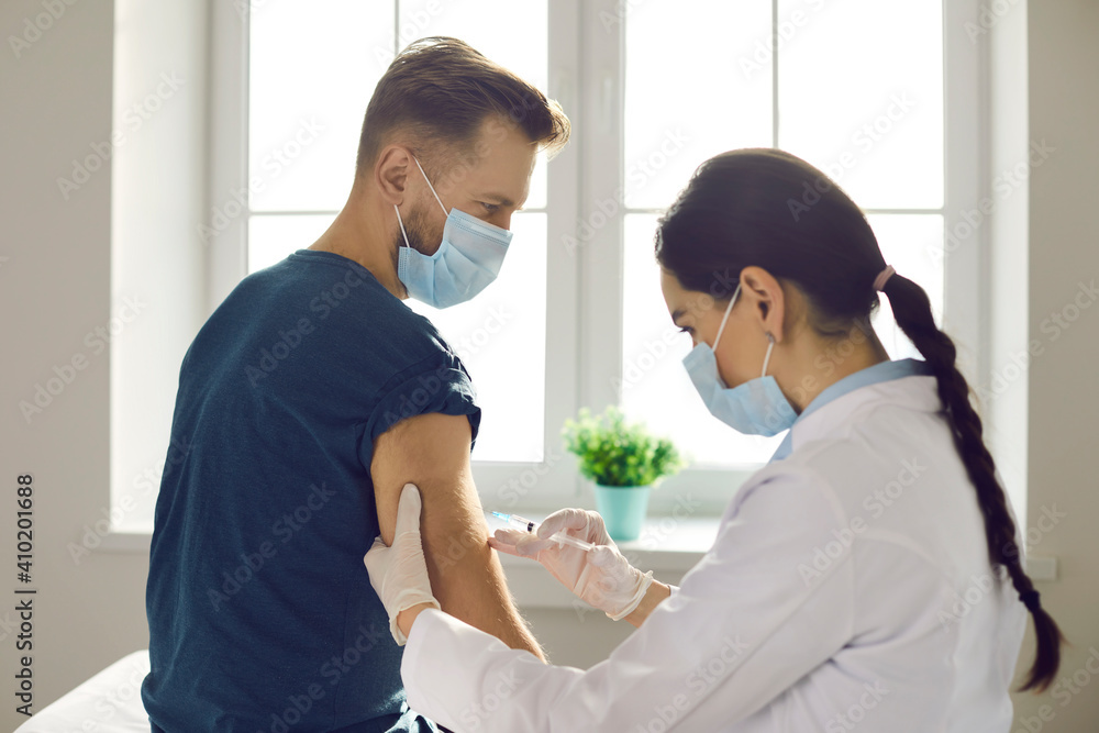 Man patient sitting in medical clinic office and getting vaccination against 19-ncov infection from woman doctor nurse over window. Vaccinating against COVID-19 infection concept Man patient sitting in medical clinic office and getting vaccination against 19-ncov infection from woman doctor nurse over window. Vaccinating against COVID-19 infection concept