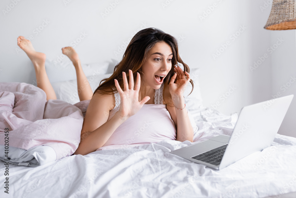 Cheerful woman having video chat on laptop on blurred foreground in bedroom Cheerful woman having video chat on laptop on blurred foreground in bedroom