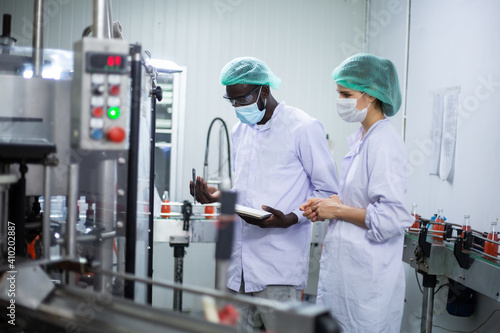 African American black man and woman worker inspecting drink product on bottling factory machinery. Process of beverage industrial concept. diversity people working together
