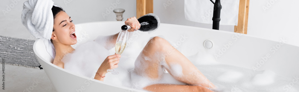 Cheerful woman pouring champagne in glass in bathtub with lather, banner - obrazy, fototapety, plakaty 