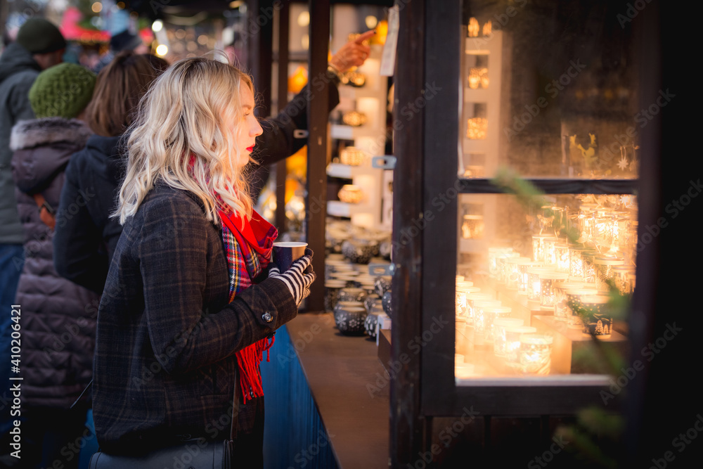 A young blonde woman browses ornate Christmas lanterns while clutching a hot drink at the Edinburgh Christmas market in Scotland.
