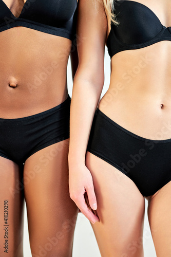 cropped two interracial women stand closely to each other have different skin color, diverse women in lingerie stand together isolated over gray studio background