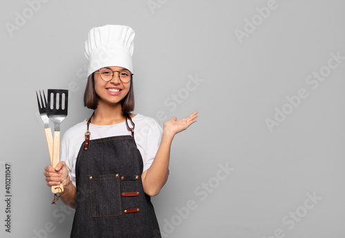 young hispanic woman smiling cheerfully, feeling happy and showing a concept in copy space with palm of hand photo