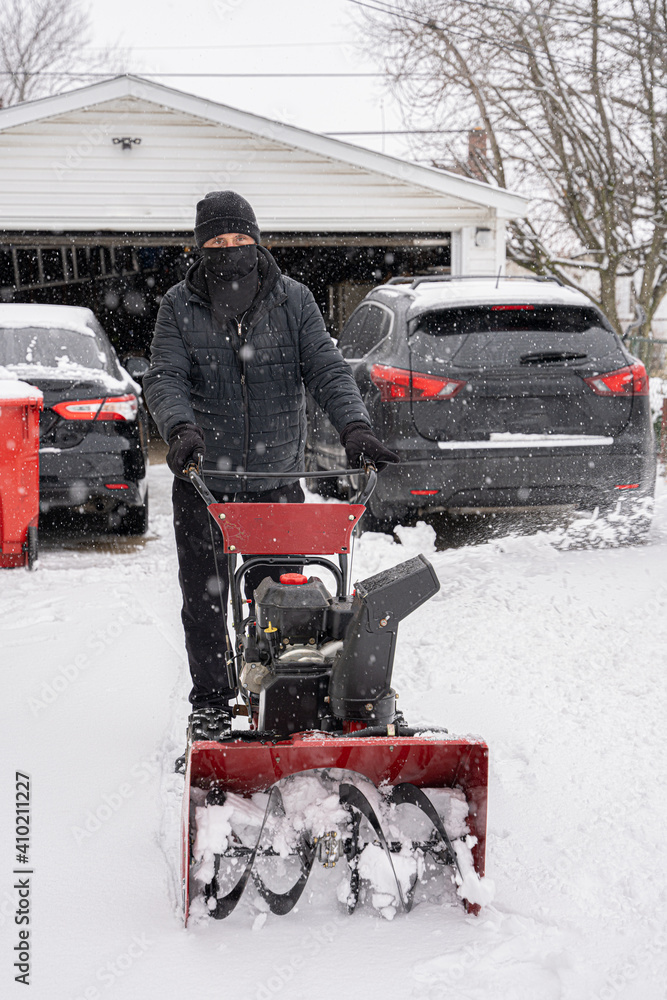 Fototapeta premium man pushes snowblower down a snowy driveway to clear the new snow fall from a recent snow storm