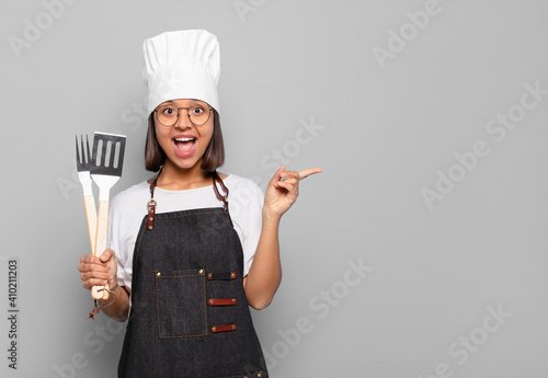 young hispanic woman looking excited and surprised pointing to the side and upwards to copy space photo