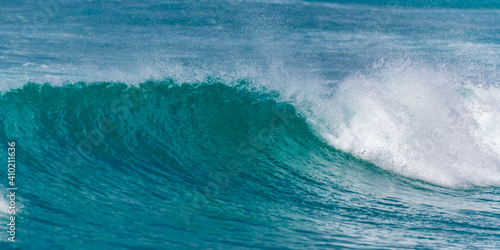 Vague qui déroule sur un spot de surf en Guadeloupe avec une mer variant du vert émeraude au bleu profond avec des embruns blancs une journée ensoleillée