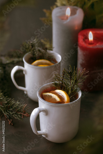 Hot aromatic winter tea with lemon slices and two candles on dark background decorated with christmas tree branches