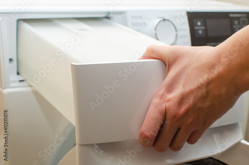 Billede på lærred A container for condensate from the dryer, a woman takes out a tank with accumulated water after drying clothes from the dryer