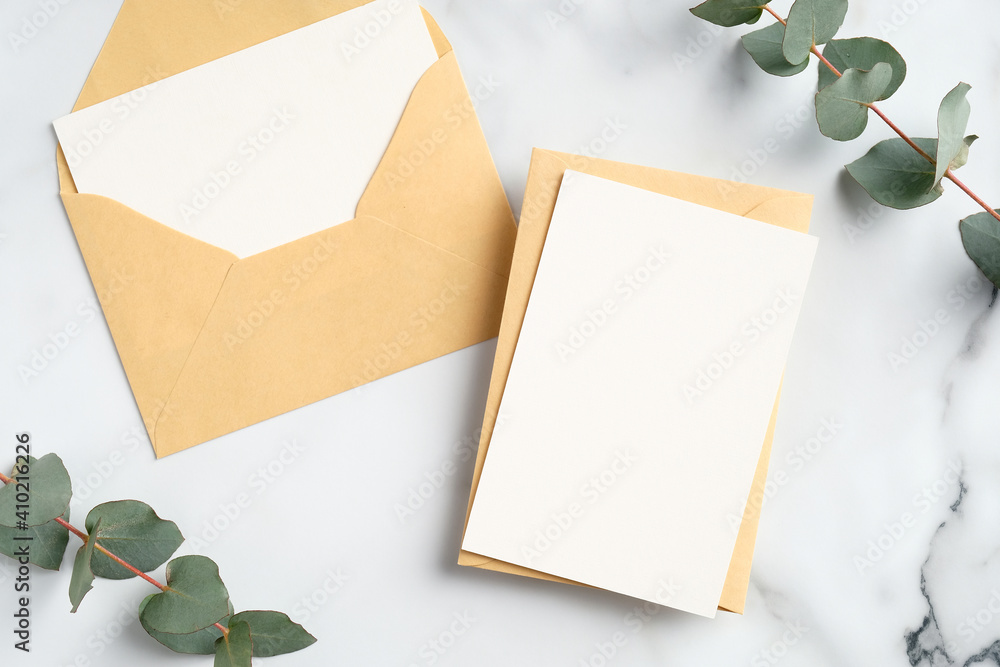 Craft paper envelopes with blank greeting cards mockups and eucalyptus leaves on marble table. Flat lay, top view. Craft paper envelopes with blank greeting cards mockups and eucalyptus leaves on marble table. Flat lay, top view.