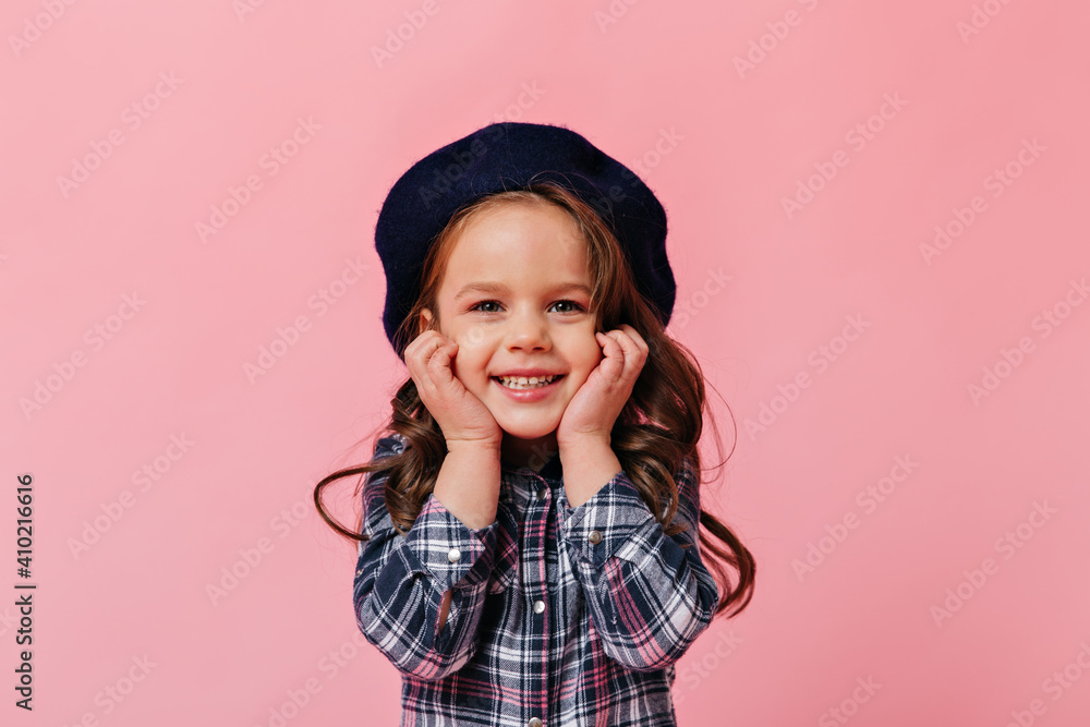Cute positive girl in beret and shirt with smile looks into camera on pink background Cute positive girl in beret and shirt with smile looks into camera on pink background