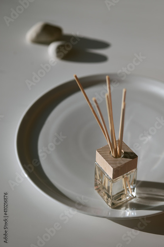 Handmade freshener with bamboo sticks diffuser and glass bottle of self made fragrance. Zen stones and aroma bottle refreshing air. Ceramic tray on simple stone table.