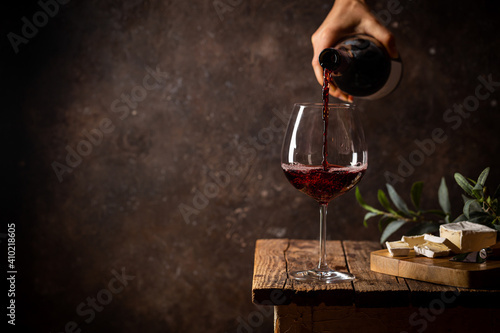 Pouring red wine into the glass against rustic dark wooden background © petrrgoskov