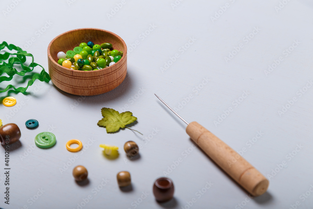 Close up of awl, box of beads and buttons, tape or ribbon for sewing and embroidery. Green and yellow set of materials for handcraft, making of bijouterie and accessories. Copy space. Close up of awl, box of beads and buttons, tape or ribbon for sewing and embroidery. Green and yellow set of materials for handcraft, making of bijouterie and accessories. Copy space.