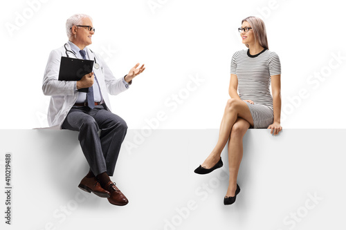 Mature doctor sitting on a blank panel and talking to a young woman