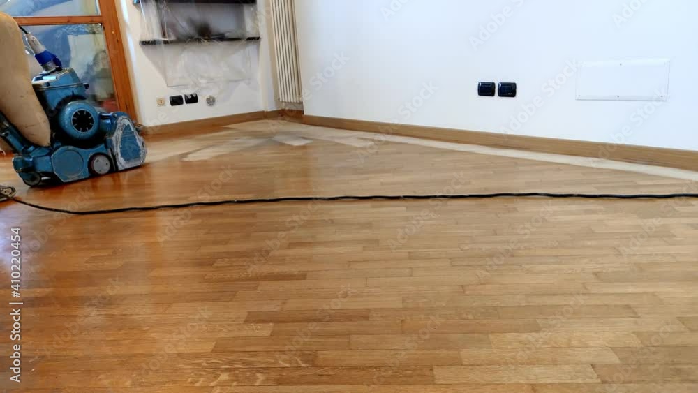 pad sander sanding hardwood floor in empty room. Man working to sand an old wooden floor to original raw oak wood. pad sander sanding hardwood floor in empty room. Man working to sand an old wooden floor to original raw oak wood.