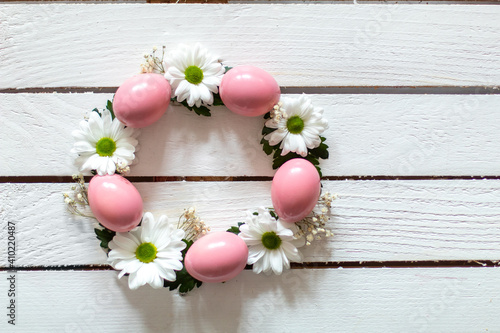 Decorative wreath of pink eggs, white flowers and green lieves on wooden table. Creative Easter concept.