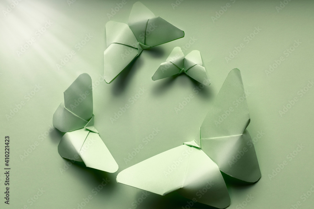 Obraz premium Butterflies of various sizes of green color from paper in origami art on isolated green background illuminated by a ray of light.