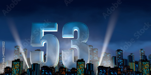 Number 53 in thick blue font lit from below with floodlights floating in the middle of a city center with tall buildings with lights on at night with cloudy sky. 3D Illustration