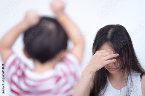 Mother closed her eyes with headache and touched forehead. While her son was shouting loudly with both hands raised.