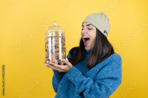 Print op canvas Young beautiful woman wearing blue casual sweater and wool hat holding chocolate