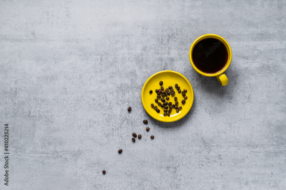 Coffee in a yellow cup. Coffee beans scattered on a gray concrete table Coffee in a yellow cup. Coffee beans scattered on a gray concrete table