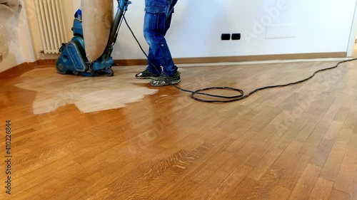 Worker man sanding oak wood floor of parquet, with pad sander machine in an empty room during a renovation. Sand and refinish hardwood floors of oak material. photo