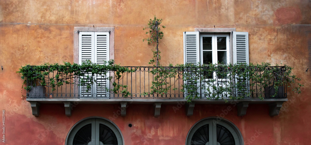 Retro, italian style orange wall with window shutters and a balcony. Romantic postcard view from small town in Italy.