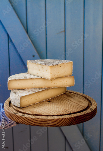 Pile of sliced french tomme cheese on a wooden board in front of a blue background photo