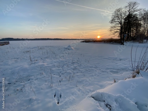 View of the frozen Białe lake near Włodawa with wooden platforms a lot of snow just before sunset elephant, orange sun like a falling comet golden hour