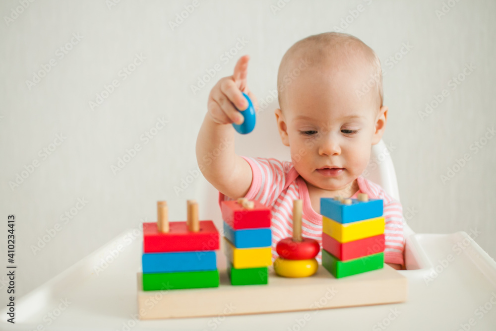 little girl plays with an educational toy - a multi-colored wooden pyramid. Development of fine motor skills and logical thinking. High quality photo little girl plays with an educational toy - a multi-colored wooden pyramid. Development of fine motor skills and logical thinking. High quality photo