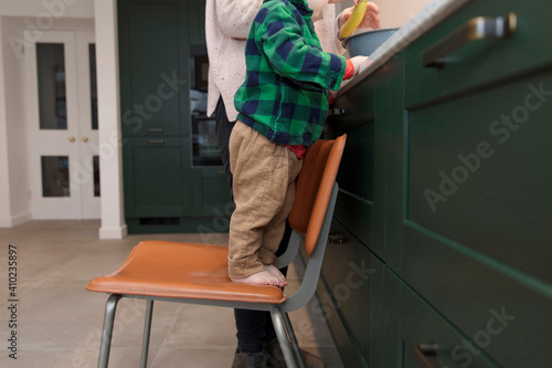 Young boy stood on a chair helping mum to bake a cake in the kitchen.