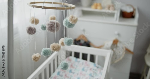 Handmade baby mobile toy hanging spinning above the crib in the bedroom. Close-up shot of multi colored nursery mobile in front of the baby changing table. Concept of childhood, new life, parenthood.
